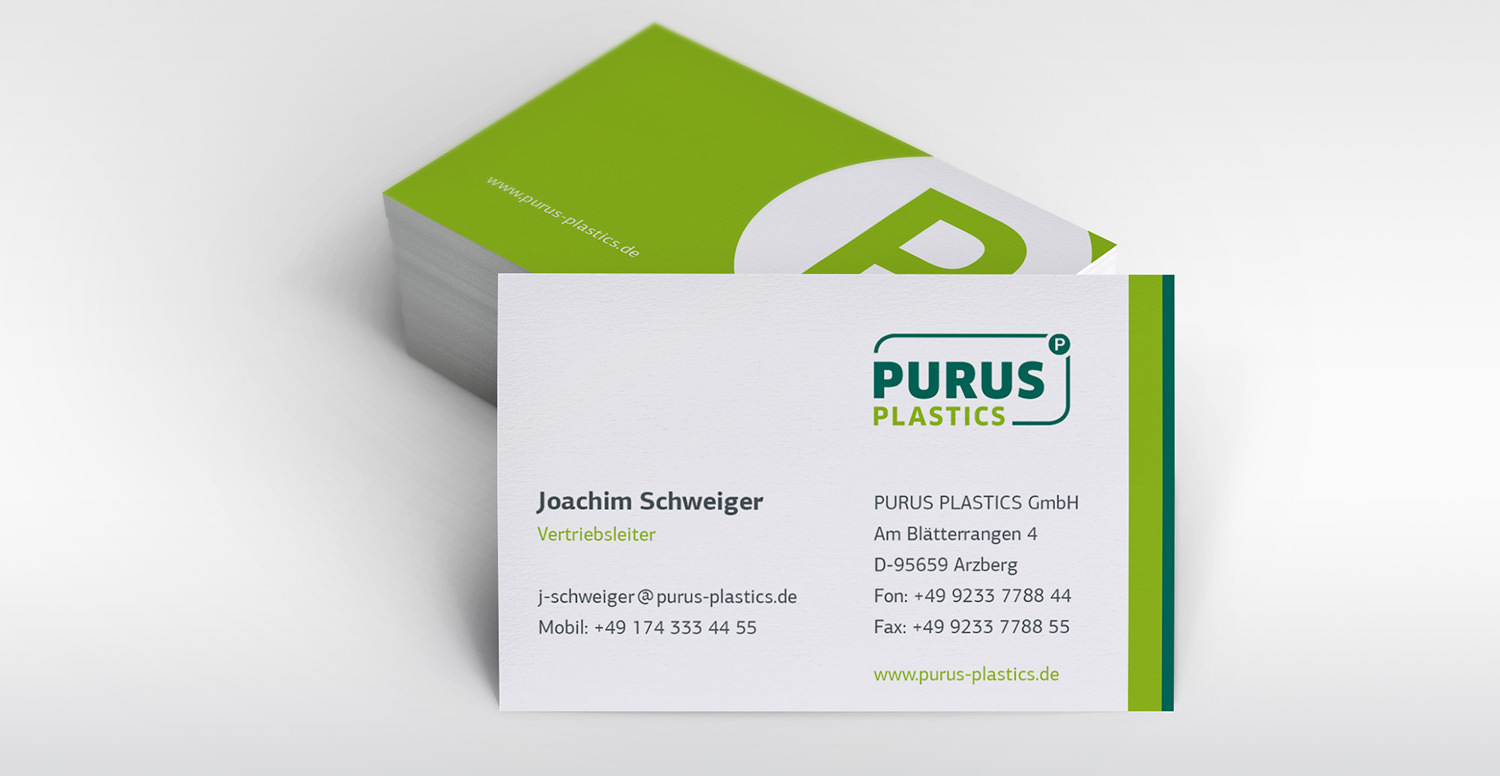 Zu sehen ist ein Stapel Visitenkarten der Firma Purus Plastics. Der Stapel zeigt die Rückseite der Karte an, während eine senkrecht aufgestellte und an den Stapel angelehnte Karte die Vorderseite der Visitenkarte in Richtung Bildbetrachter zeigt.